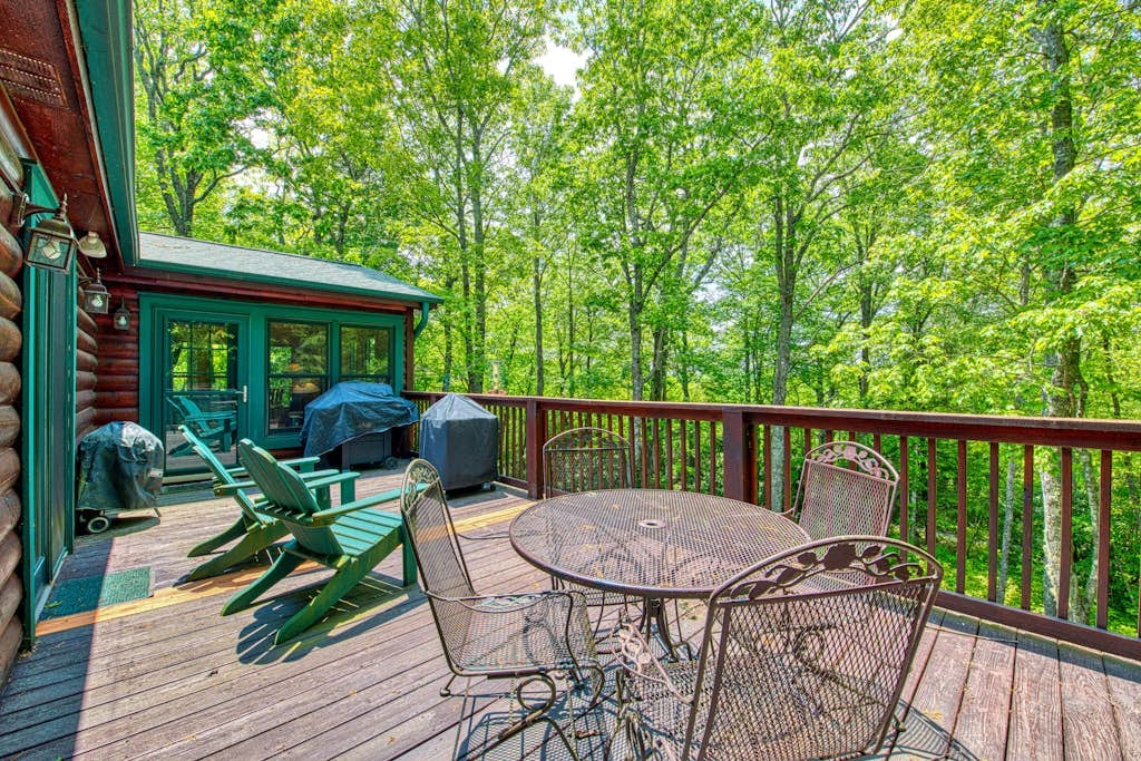 Forest-facing deck with outdoor dining table, grill, and Adirondack chairs