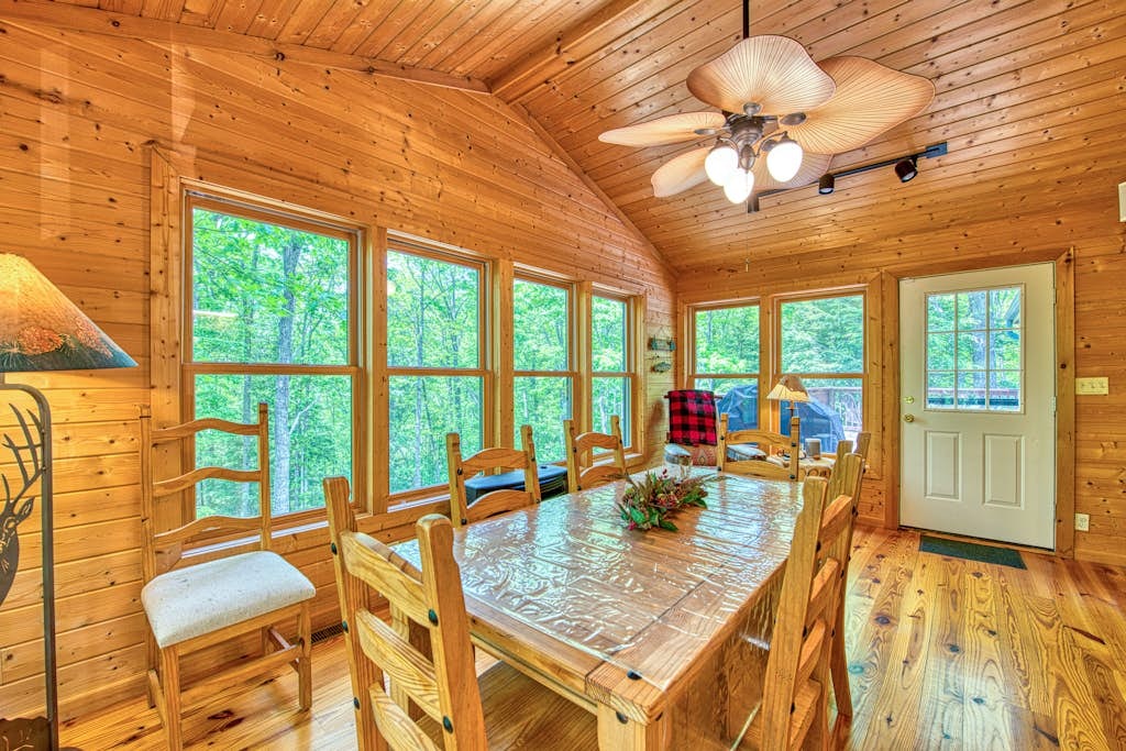 Sunlit dining room with a large wood table and windows overlooking the forest