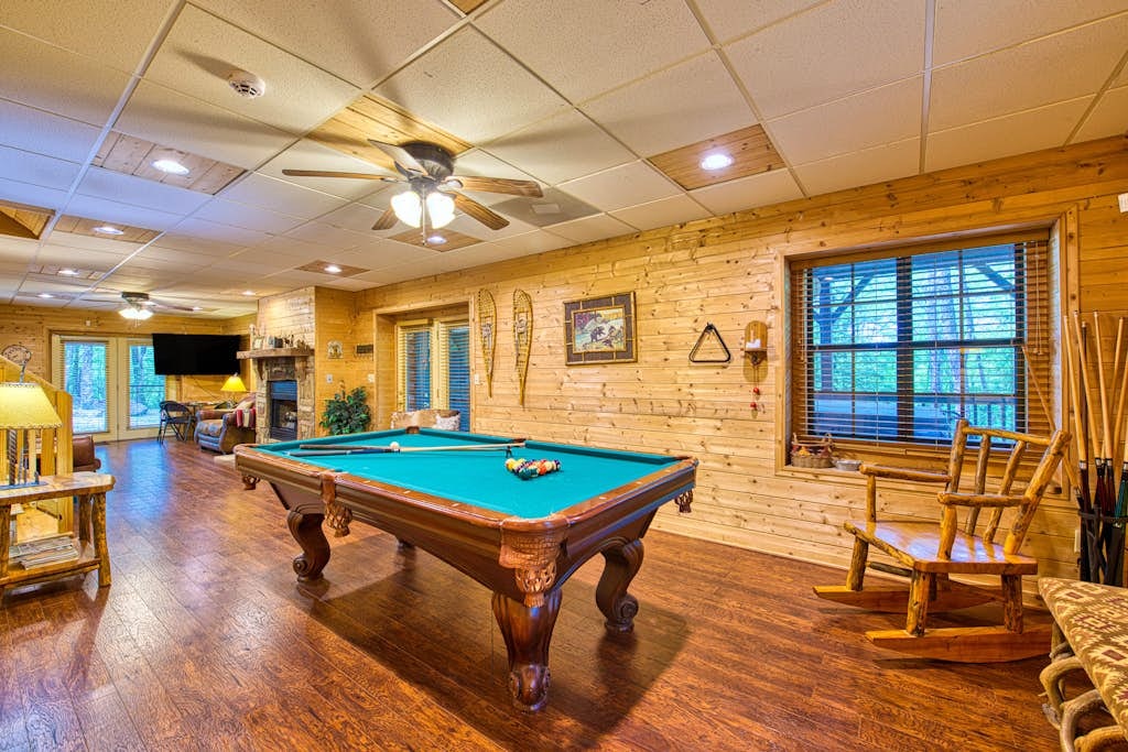 Lower-level game room with pool table, rocking chairs, and woodland views
